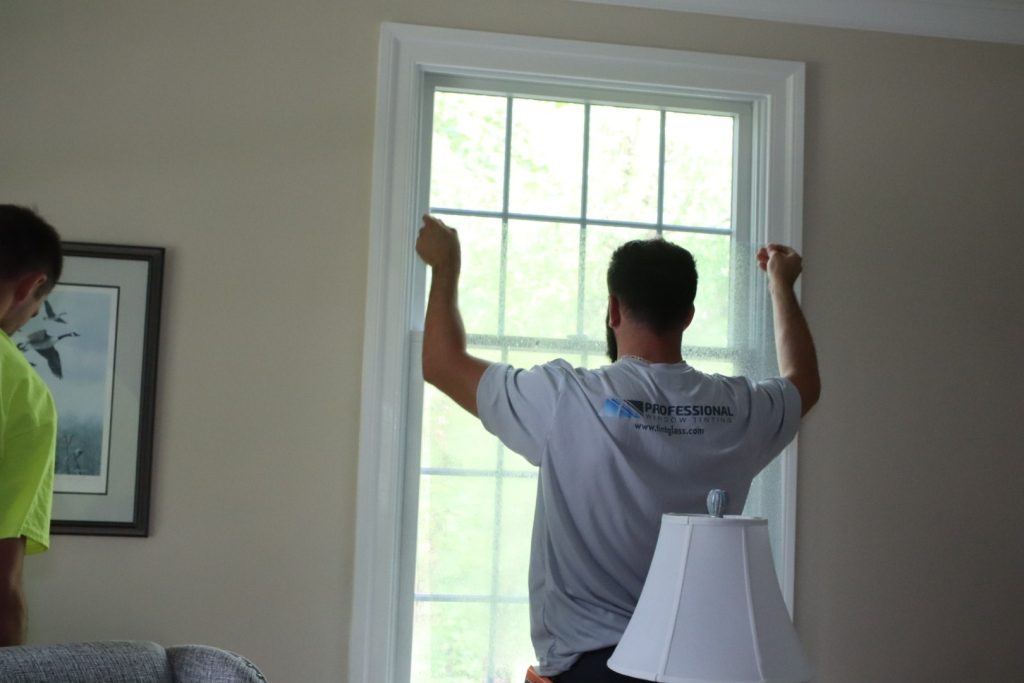 An installer from Professional Window Tinting adds efficiency and energy savings to a home by adding window film to the existing insulated windows.