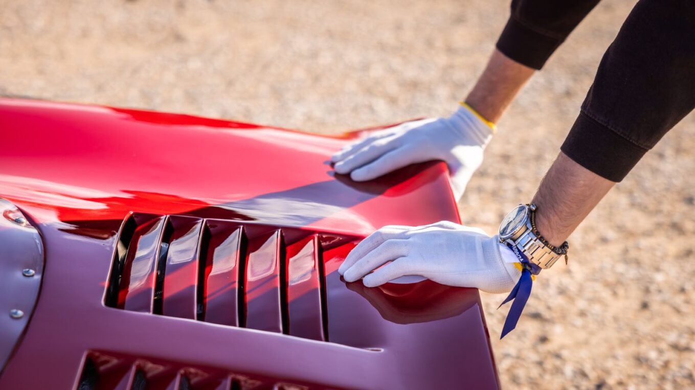 Gloved hands wiping down a red car hood, the kind of finish paint protection film is meant to keep clear